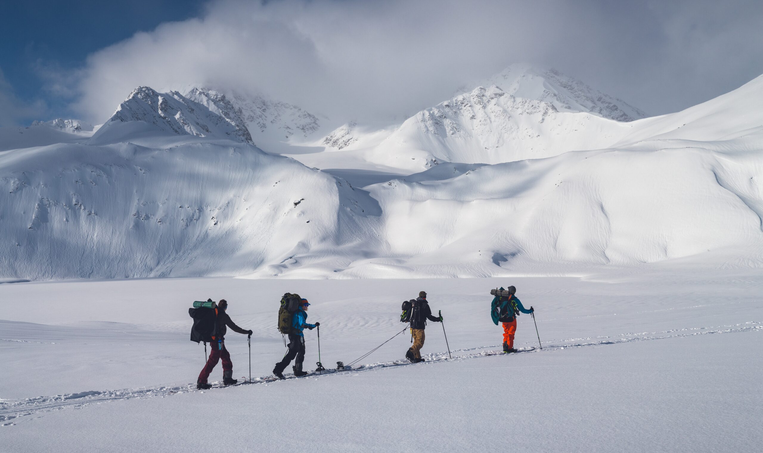A horizontal shot of a group of people hiking in the mountains covered in snow under the cloudy sky